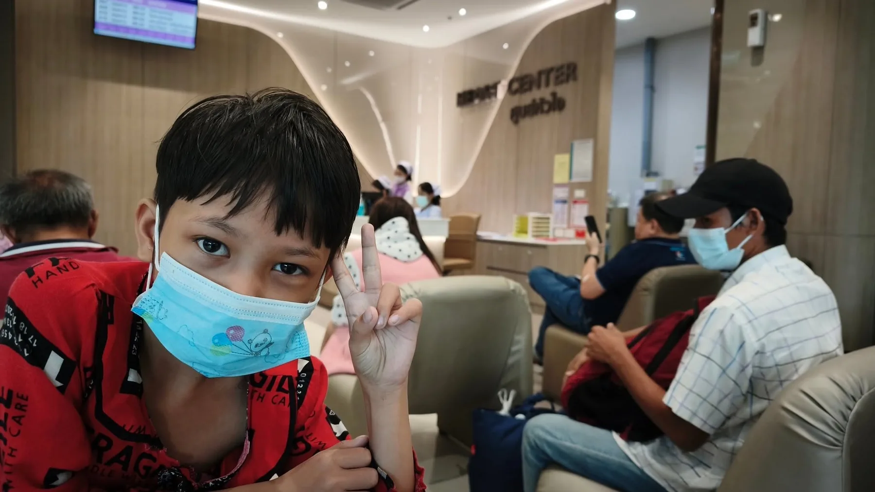 Lin Lin Htet dans la salle d'attente de l'hôpital à Bangkok, masque sur le visage, faisant le signe de la victoire