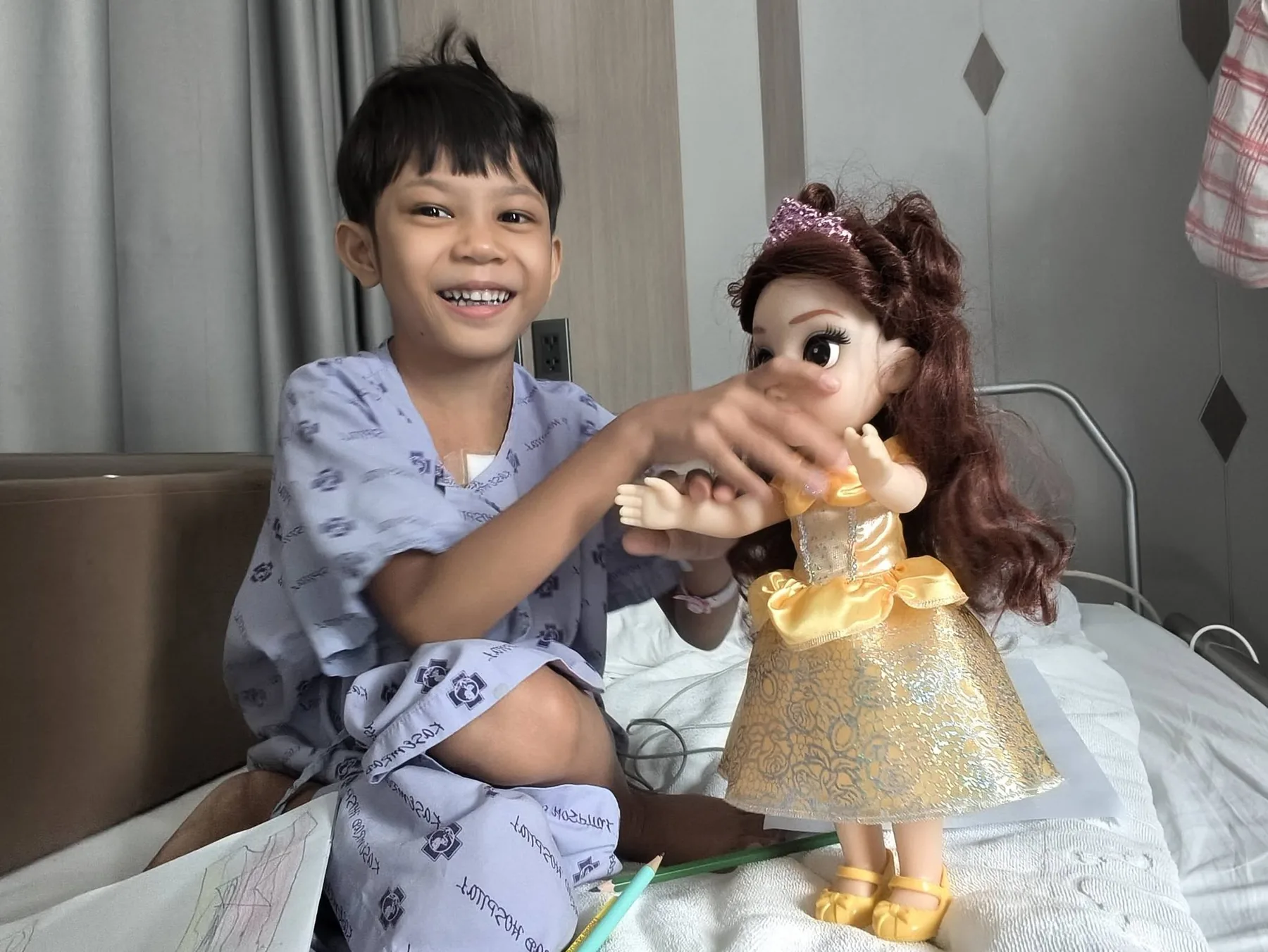 Lin Lin Htet assise sur son lit d'hôpital, rayonnante, jouant avec une poupée