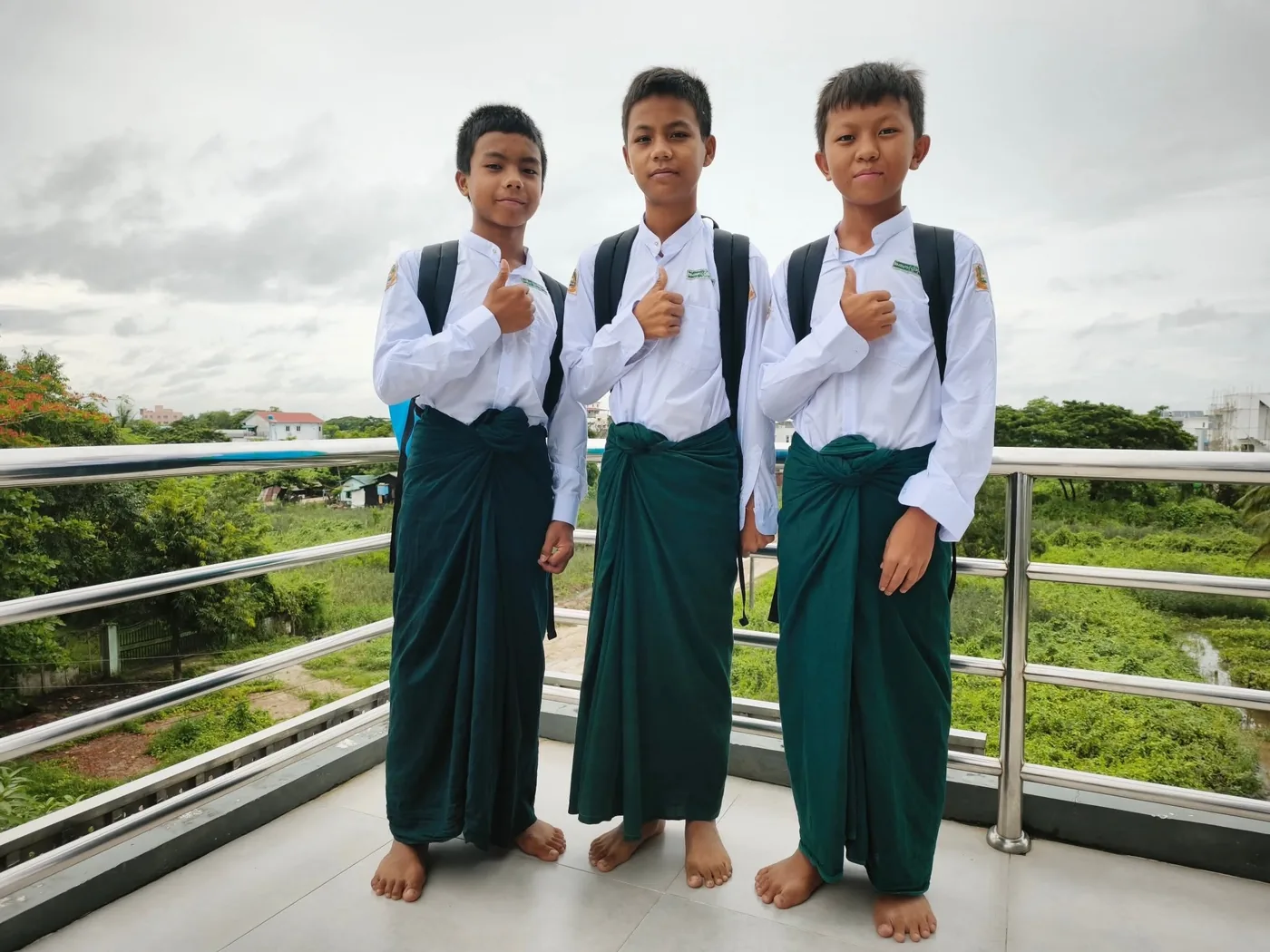 Three boys in uniform on the terrace of the boarding house, giving a thumbs up